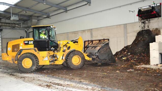 Lkw mit Schaufel arbeitet in einer Halle und bewegt einen großen Haufen organischer Abfälle.