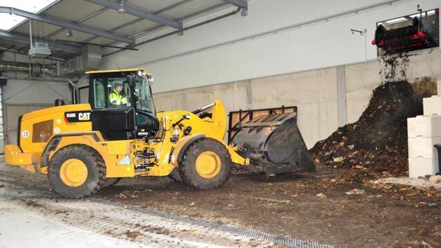 Lkw mit Schaufel arbeitet in einer Halle und bewegt einen großen Haufen organischer Abfälle.