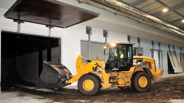 Gelber Radlader fährt gerade in eine Lagerhalle und hebt Schutt mit seiner Schaufel in den Innenraum.
