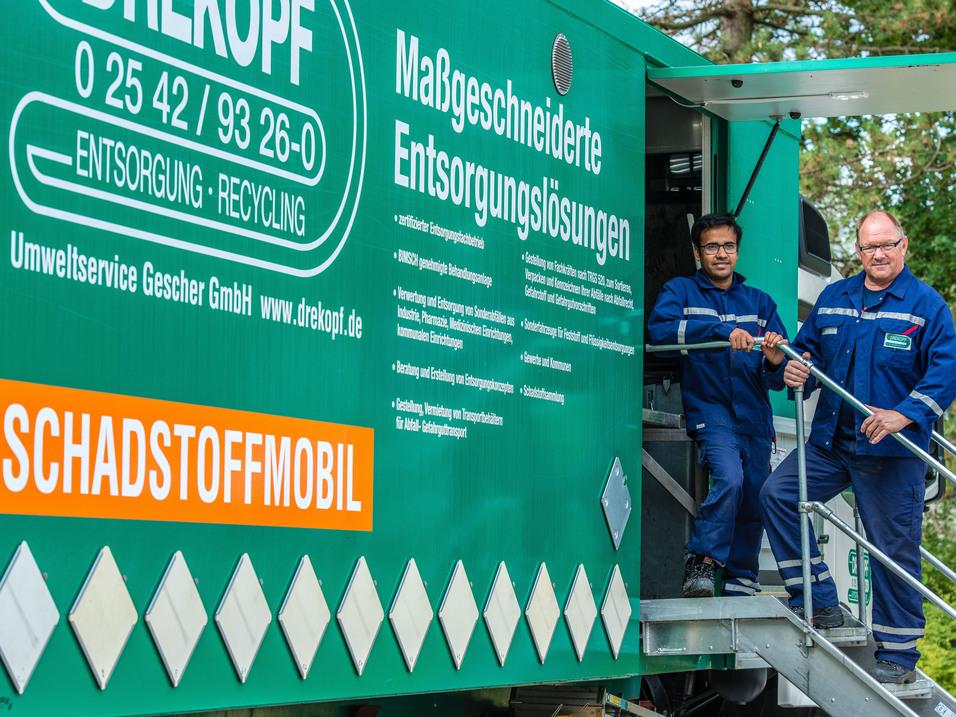 zwei M&auml;nner stehen auf einer Metalltreppe, die in einen gr&uuml;nen LKW f&uuml;hrt. Der LKW ist das Schadstoffmobil.
