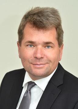 Porträt eines Mannes mit kurzer, grauer Frisur, Anzug und Krawatte, vor einem neutralen Hintergrund.