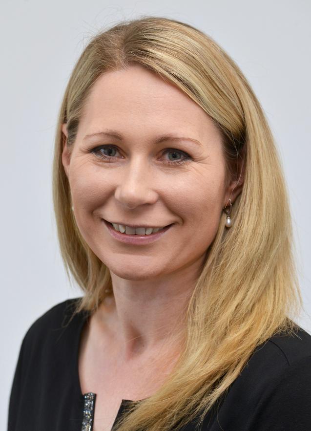 Porträt einer Frau mit blonden, langen Haaren, die in ein schwarzes Oberteil gekleidet ist und freundlich lächelt.