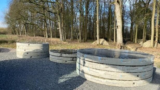 Große Betonringe lagern auf einer abgeschotterter Fläche. Wald im Hintergrund.