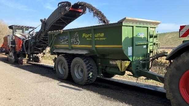 Ein Granualt wird mit einer Art Förderband auf den Anhänger eines Traktors gekippt.