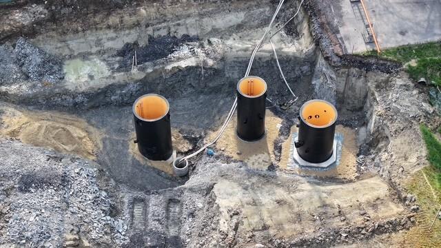 3 große, schwarze Rohre ragen aus einer Baugrube heraus.